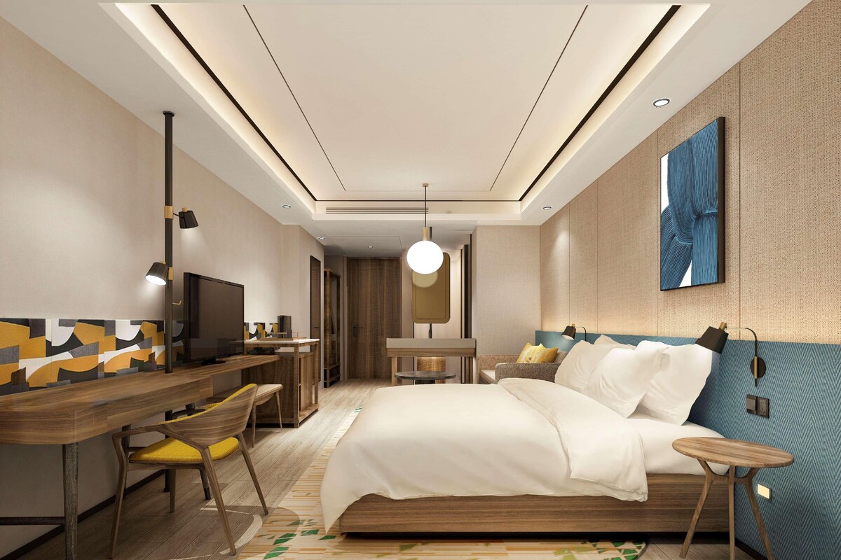 A modern hotel room with a bed, desk, and seating area.