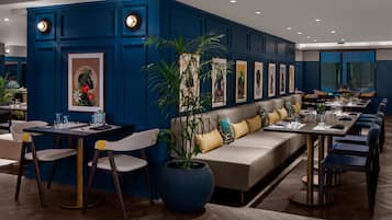 A modern dining area with a blue accent wall, a large potted plant, and a long communal table with chairs.