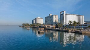 A waterfront hotel with multiple high-rise buildings, a marina with boats, and palm trees along the shore.