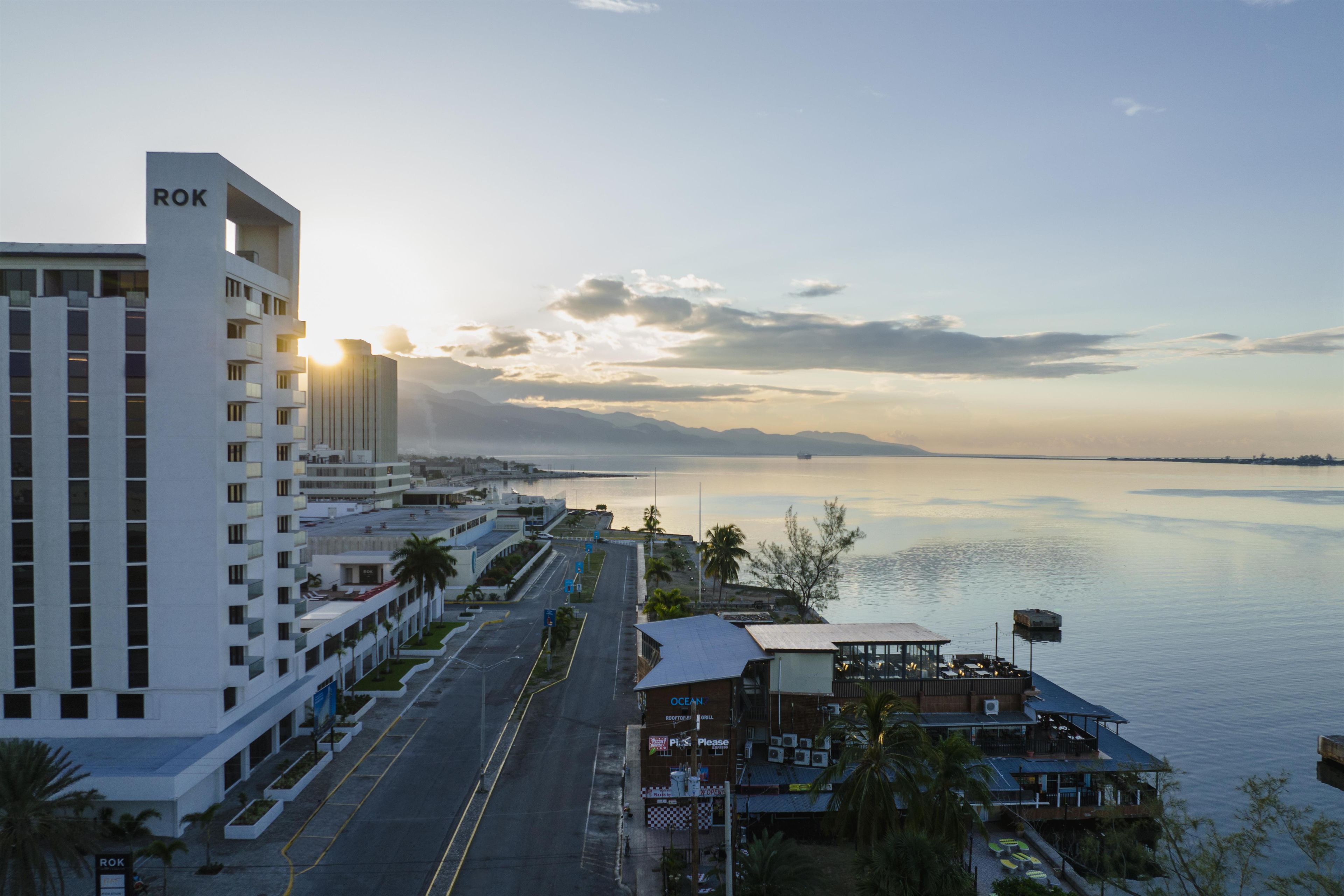 Un paisaje urbano costero con un edificio blanco destacado identificado como 'ROK' y un muelle tranquilo.