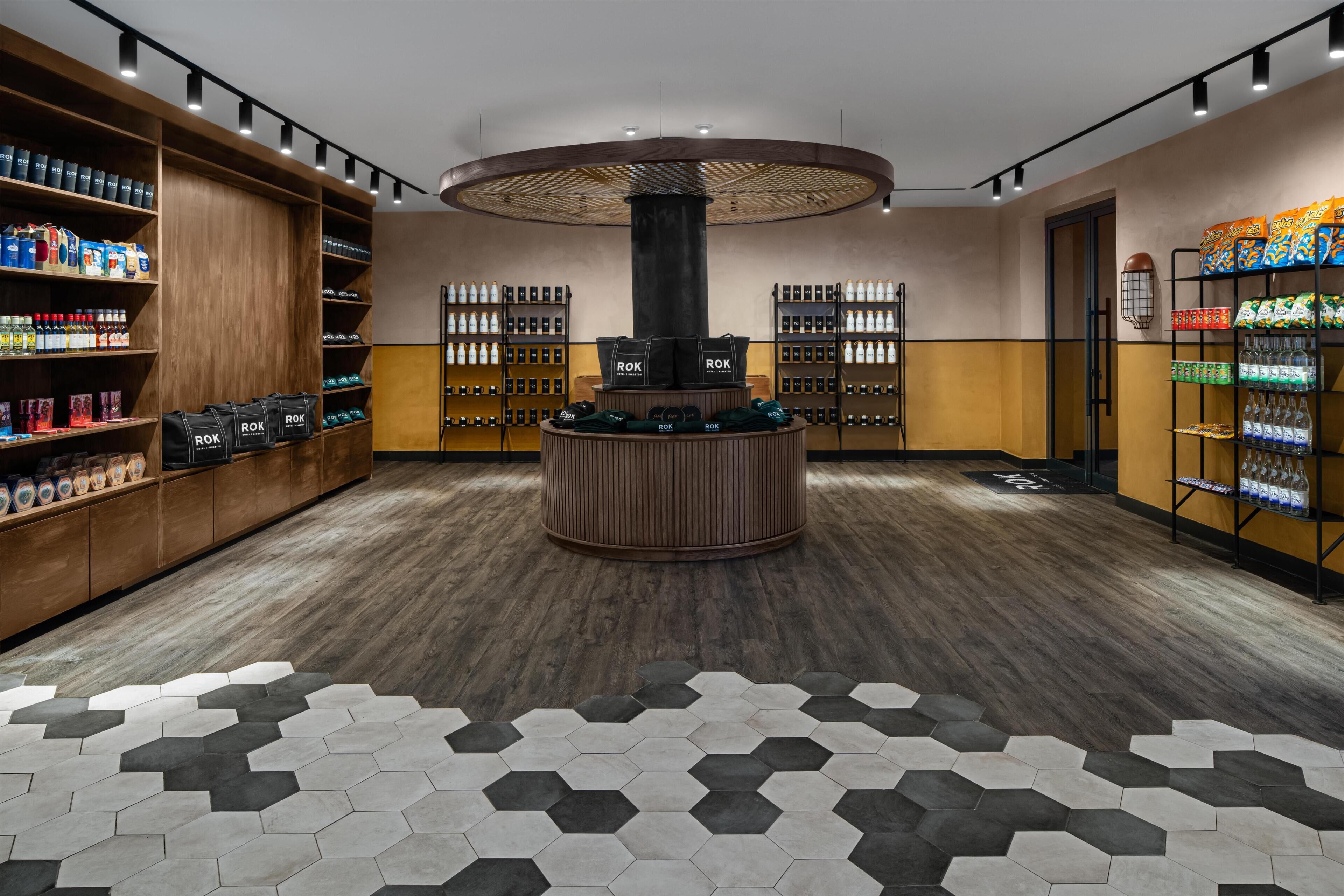 A hotel lobby with wooden shelving, a central circular column, hexagonal patterned flooring, and various packaged goods on shelves.