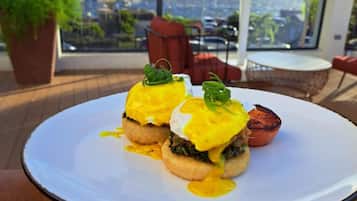 A table with two eggs benedict dishes on a white plate, set on a wooden deck with a city view in the background.