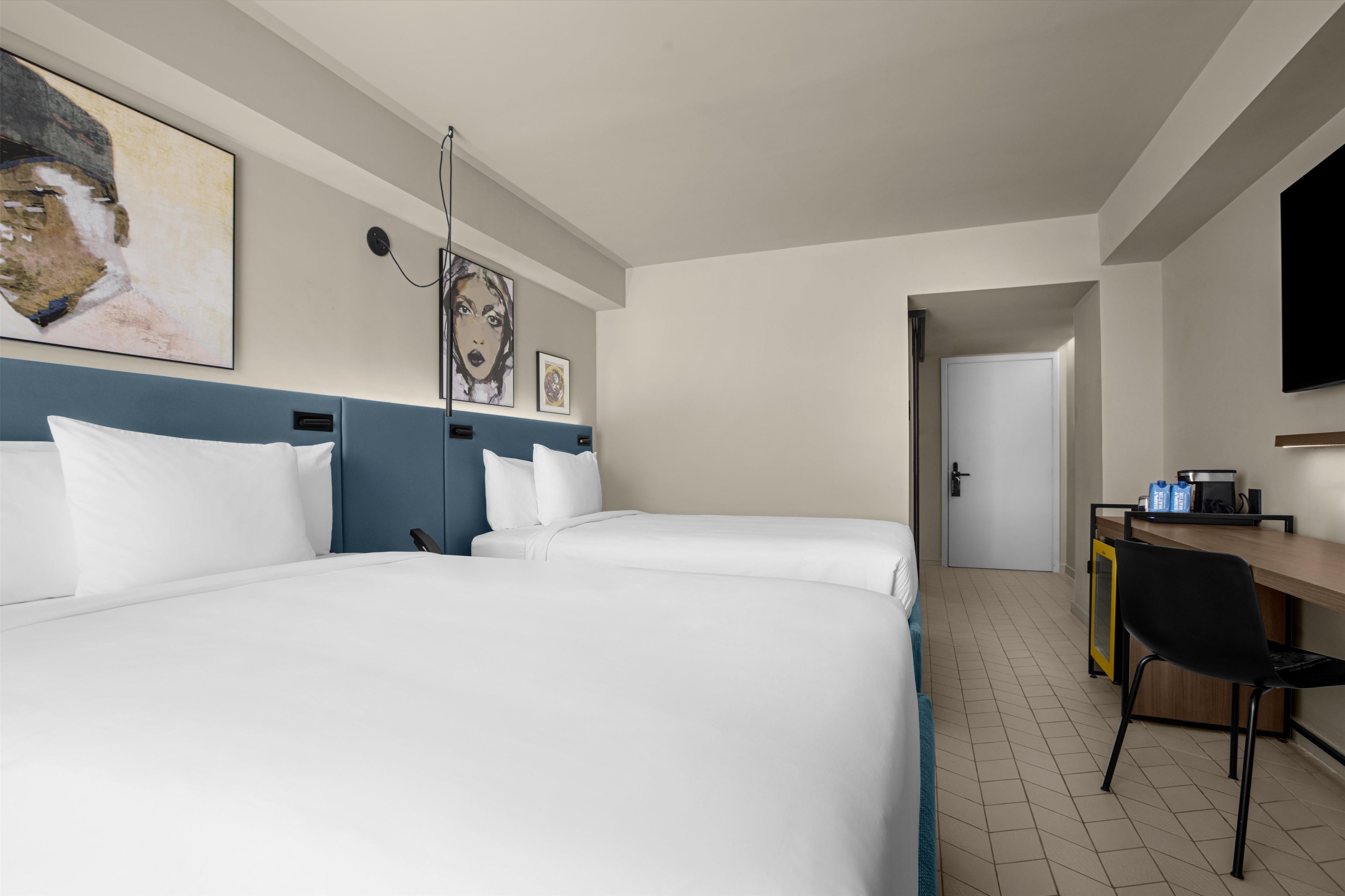 A hotel room with two beds, a desk, a chair, and a television.