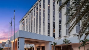 A modern hotel with a large entrance, multiple floors, and a covered area with palm trees.