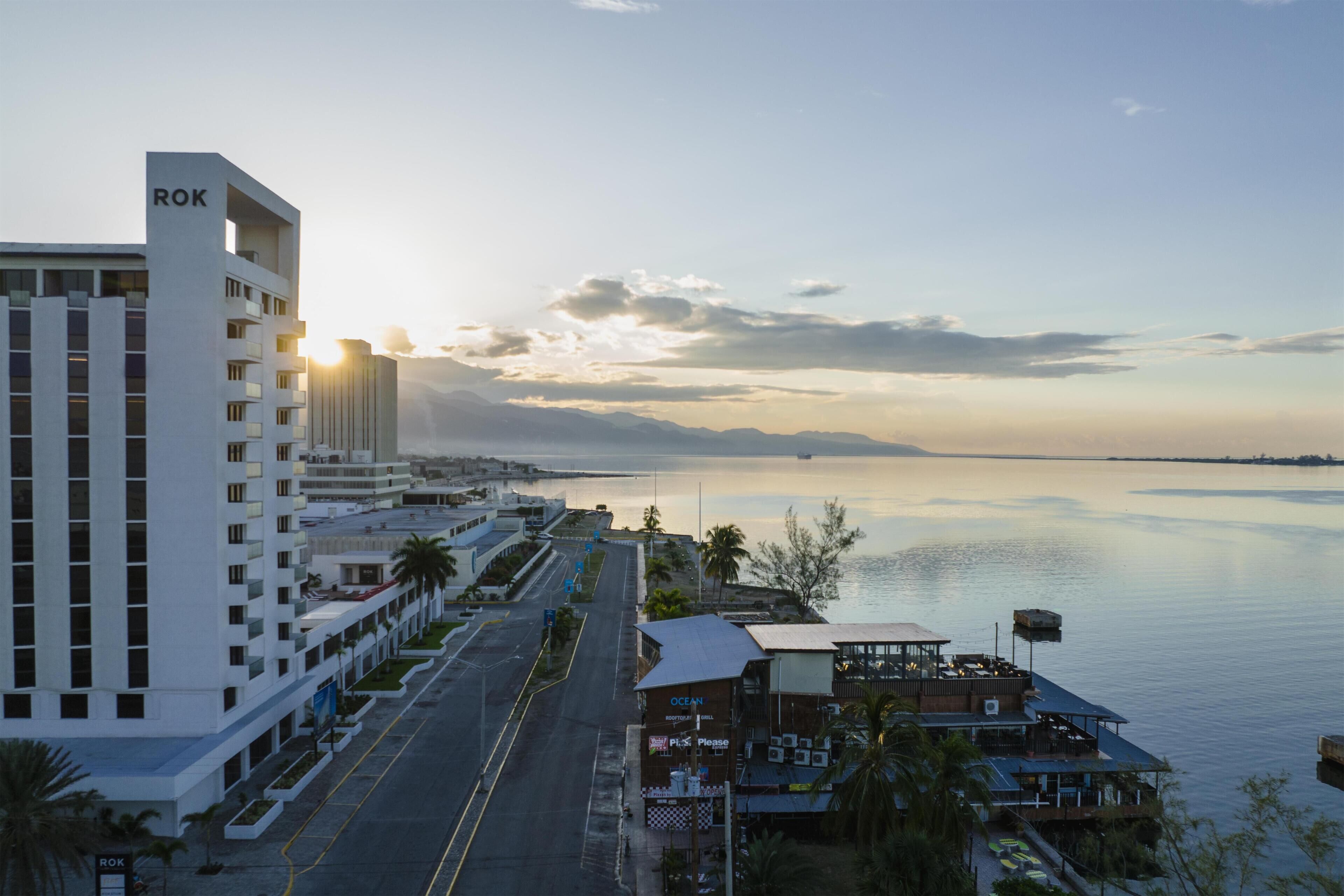 A waterfront hotel with a prominent 'ROK' sign, a long road with palm trees, and a calm sea.