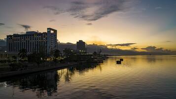 A waterfront hotel with a view of the sunset, calm water, and distant mountains.