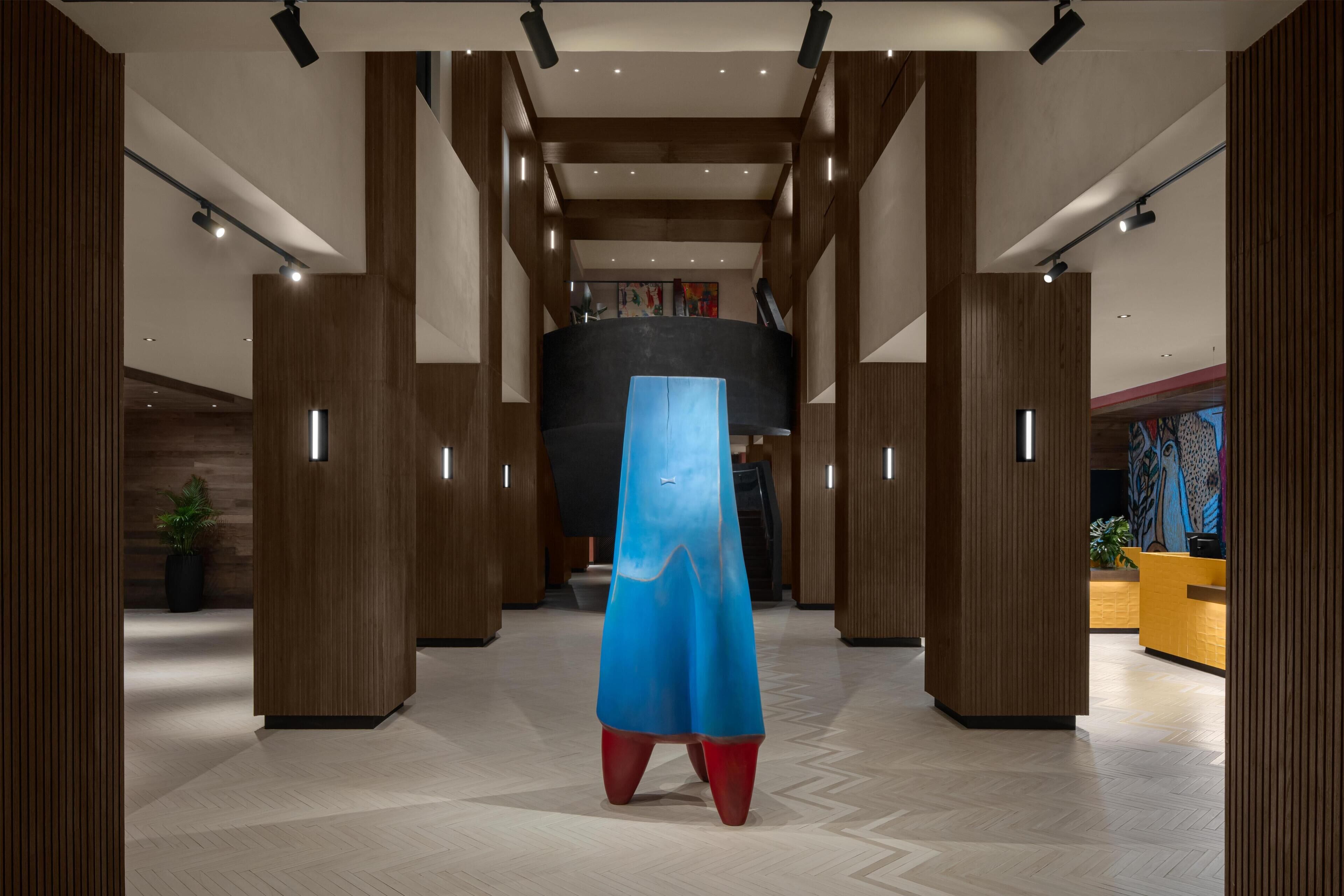 Un vestíbulo moderno con paneles de madera, una escultura azul en el centro y un mostrador de recepción.