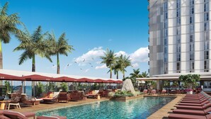 A hotel pool area with lounge chairs, umbrellas, and palm trees.
