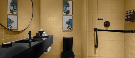 A bathroom with a black sink, toilet, and shower area, featuring yellow walls and artwork.