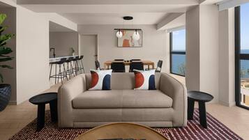 A modern living room with a sofa, dining table, and chairs, a kitchen area, and large windows with a view.