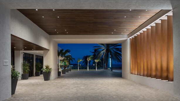 A modern building with a wooden ceiling, large potted plants, and a view of palm trees at dusk.