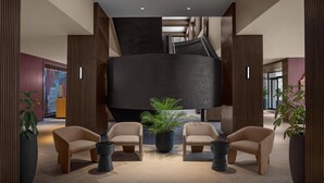 A modern lobby with a central black structure, wooden paneling, and seating areas with potted plants.
