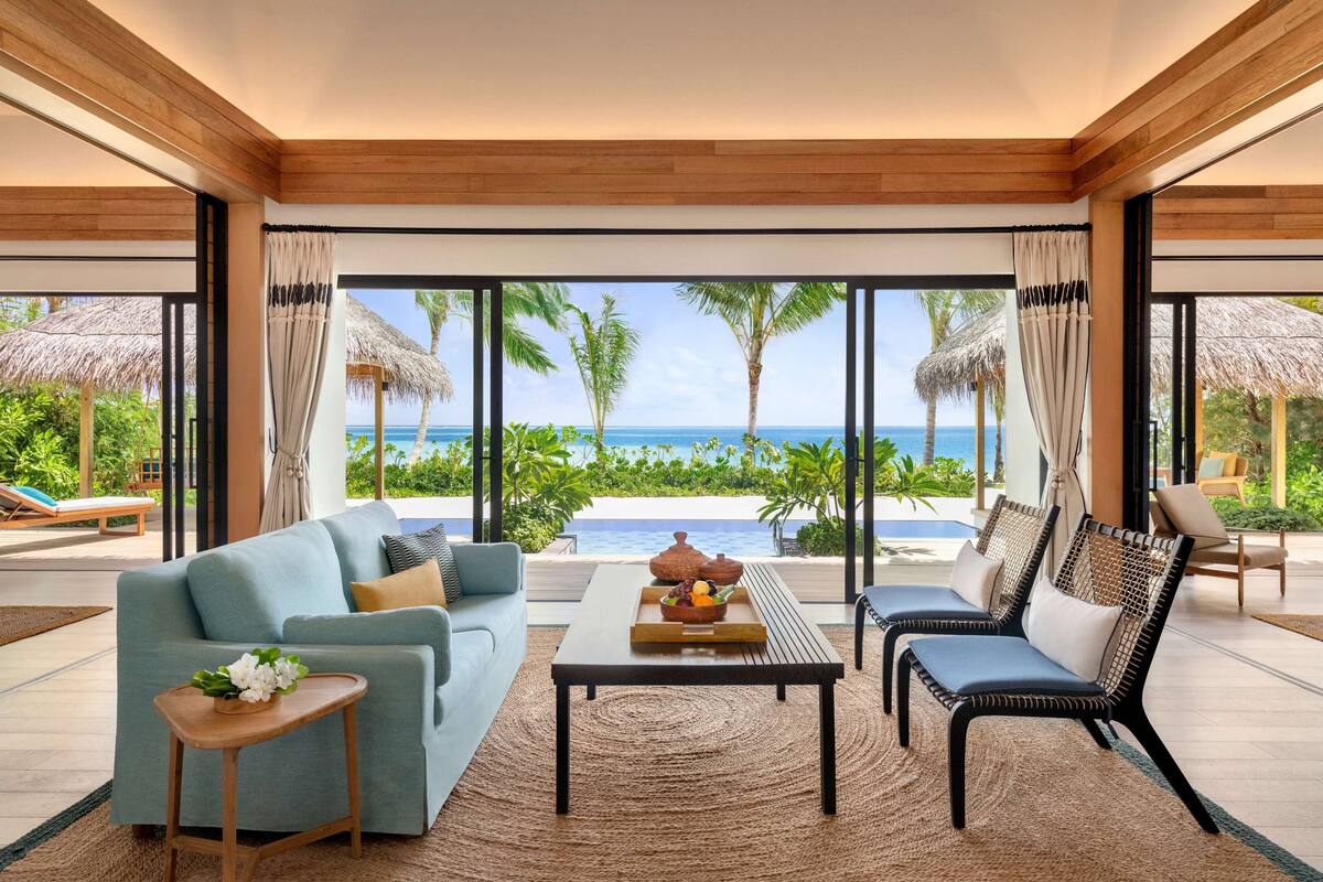 Ein modernes Wohnzimmer mit einer Couch, einem Couchtisch und zwei Sesseln, mit Blick auf einen Pool und den Ozean.