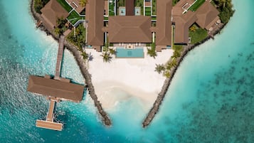 Een luchtbeeld van een resort in een hartvormige indeling, met een centraal zwembad, meerdere gastvillas en een strand.