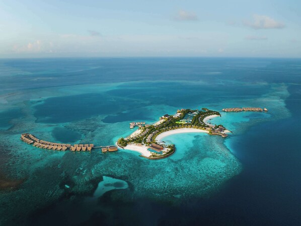 An aerial view of a resort island with overwater bungalows, a central building, and a crescent-shaped beach. - Hilton Maldives Amingiri Resort & Spa (Amingiri)
