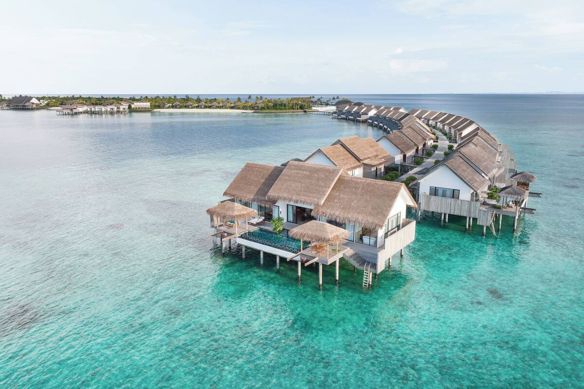 Ein Resort mit Bungalows über dem Wasser, mit Reetdächern, klarem türkisblauem Wasser und Blick auf den Ozean.