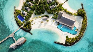Vue aérienne d’un complexe hôtelier comprenant une grande piscine, plusieurs villas et une jetée.