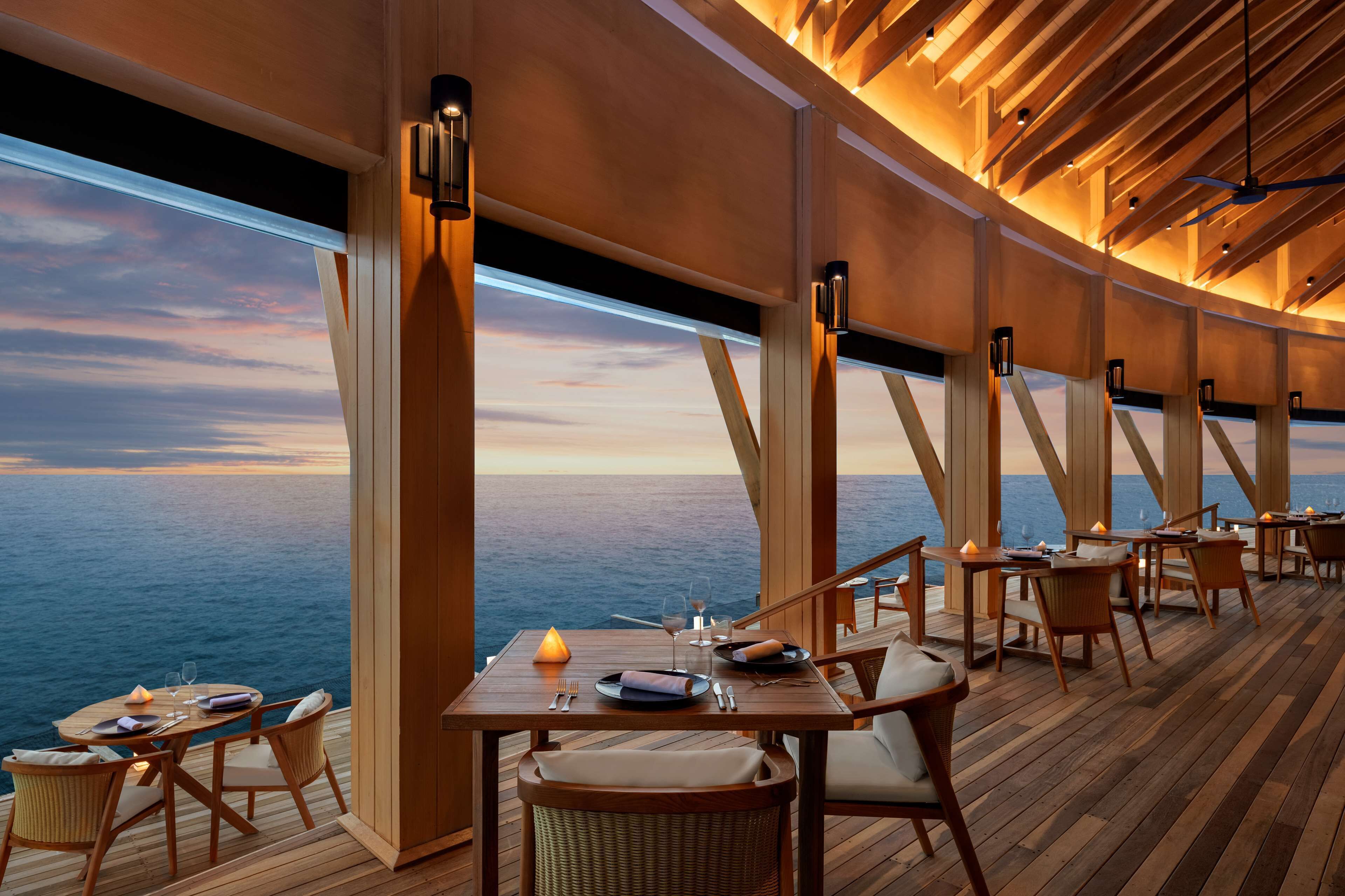 A dining area with tables and chairs, a view of the ocean, and wooden beams on the ceiling.