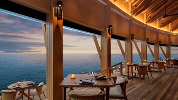 A dining area with tables and chairs, a view of the ocean, and wooden beams on the ceiling.