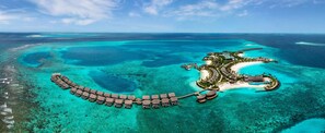 An aerial view of a resort with overwater bungalows, a beach, and clear turquoise waters.