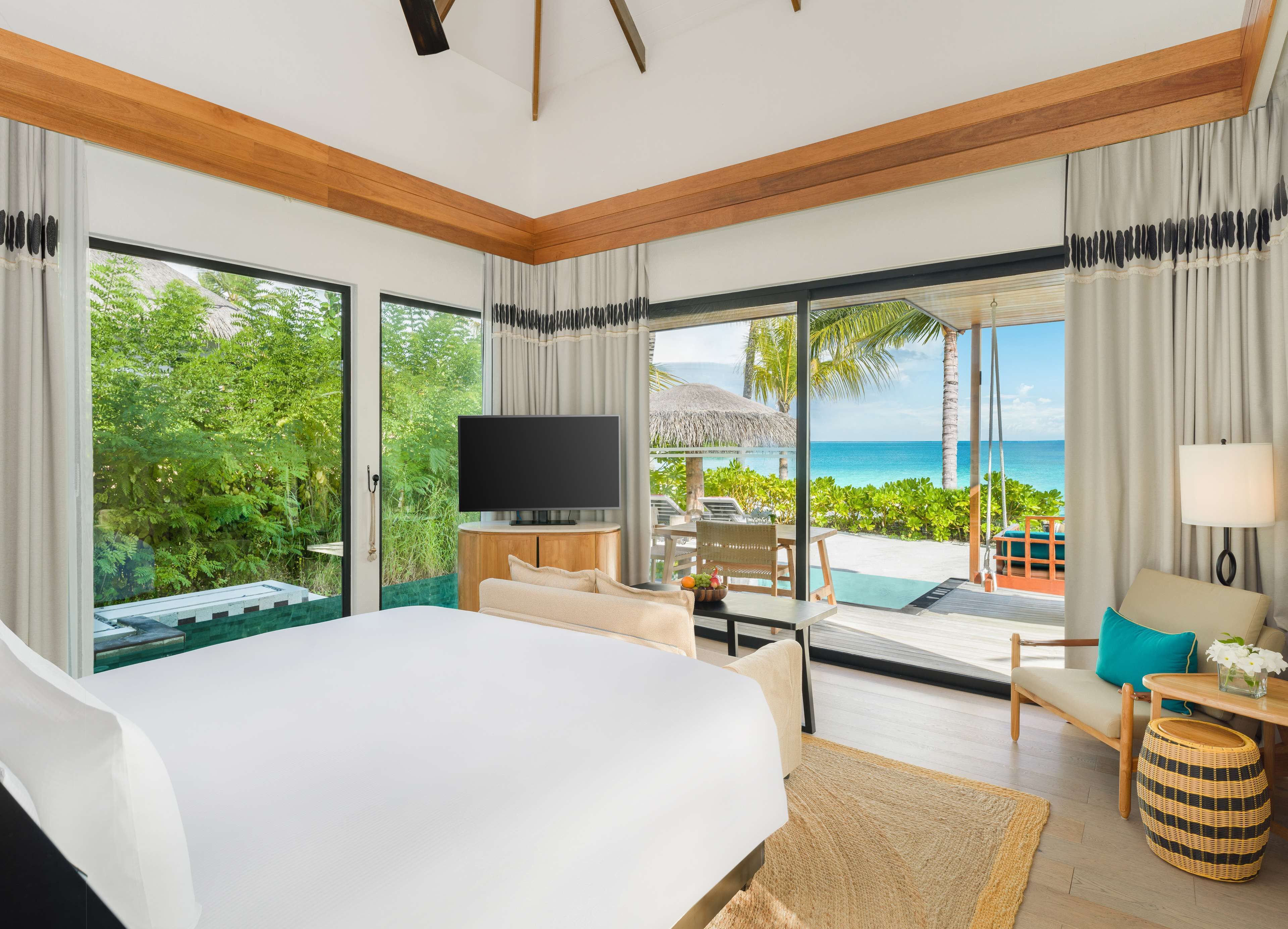 A hotel room with a large bed, a TV, a dining area with a table and chairs, and a view of the ocean.