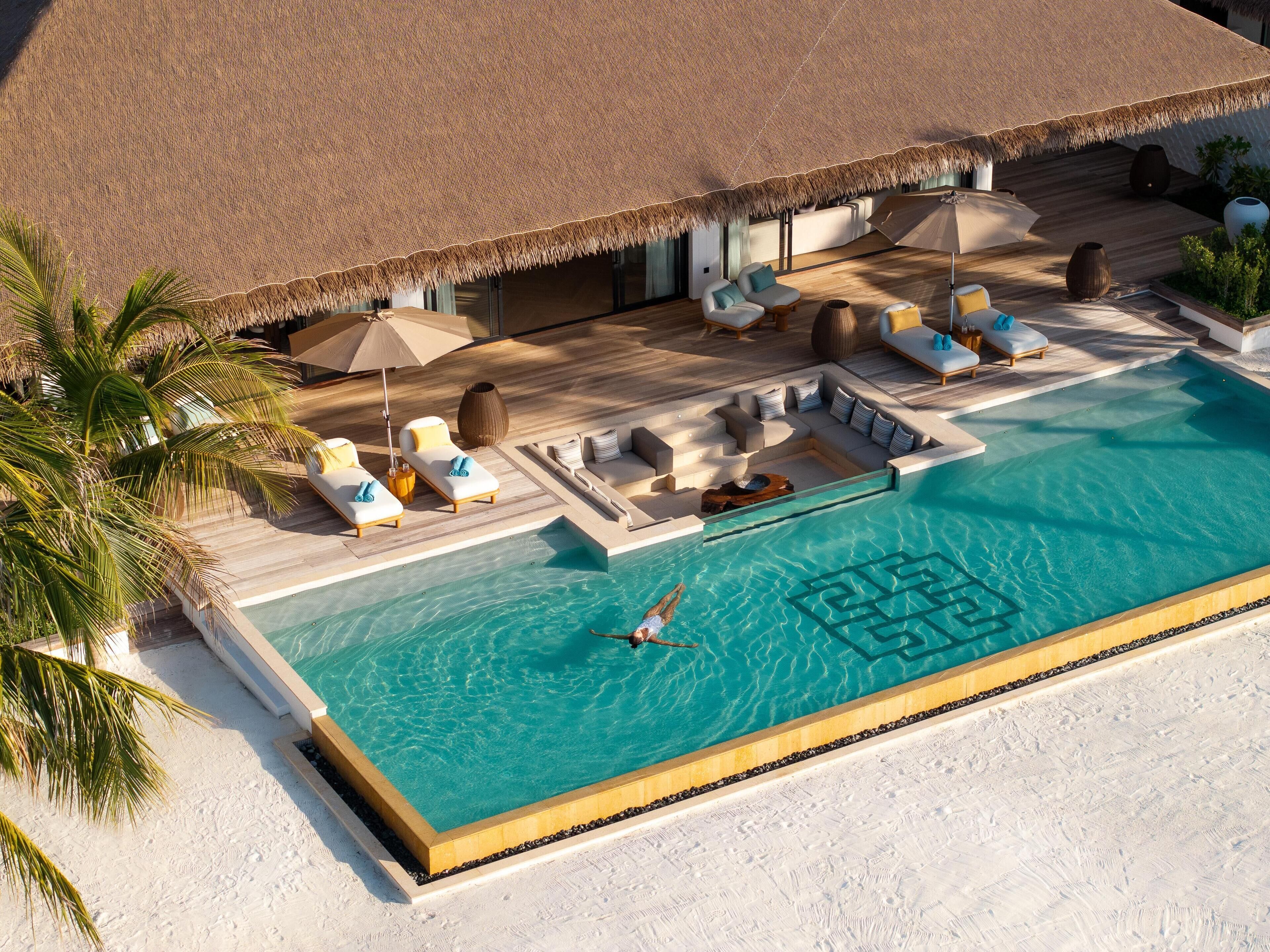 A poolside area with lounge chairs, a swimming pool, and a thatched roof structure.