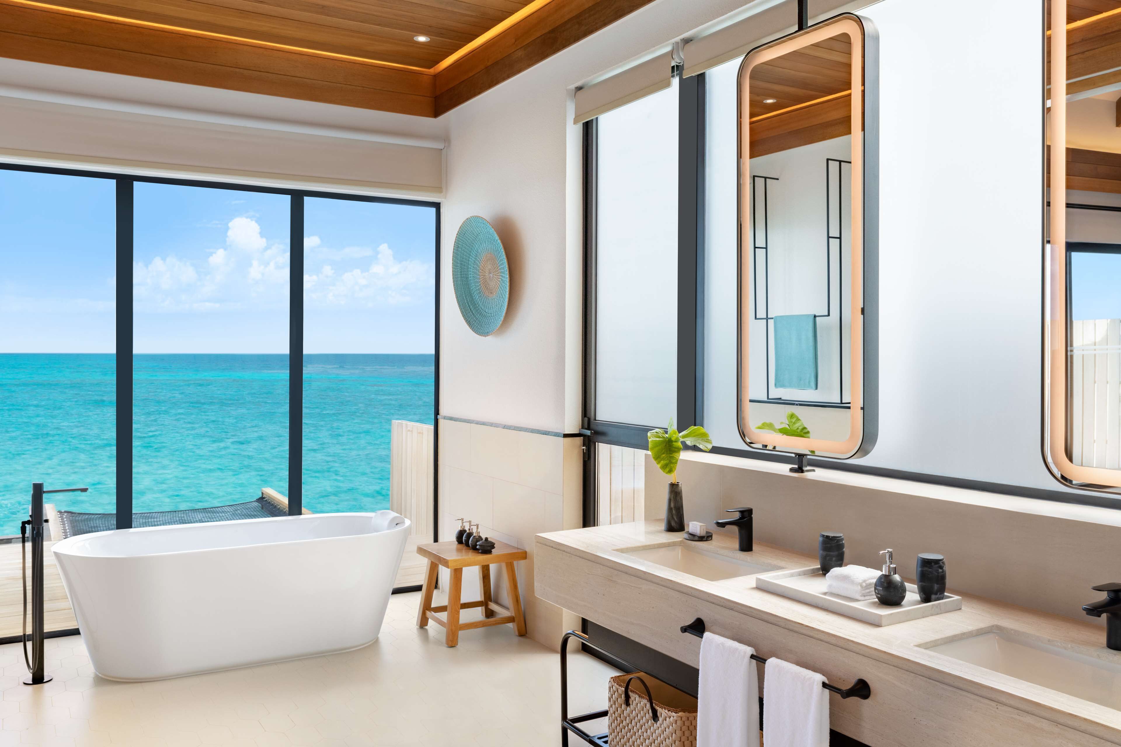A modern bathroom with a freestanding bathtub, a large mirror, and a view of the ocean.
