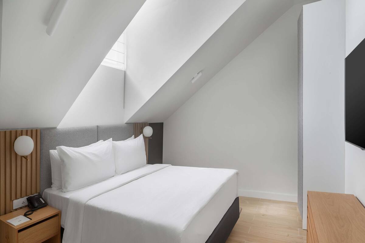 A modern hotel room with a bed, bedside table, and a flat-screen TV mounted on the wall.