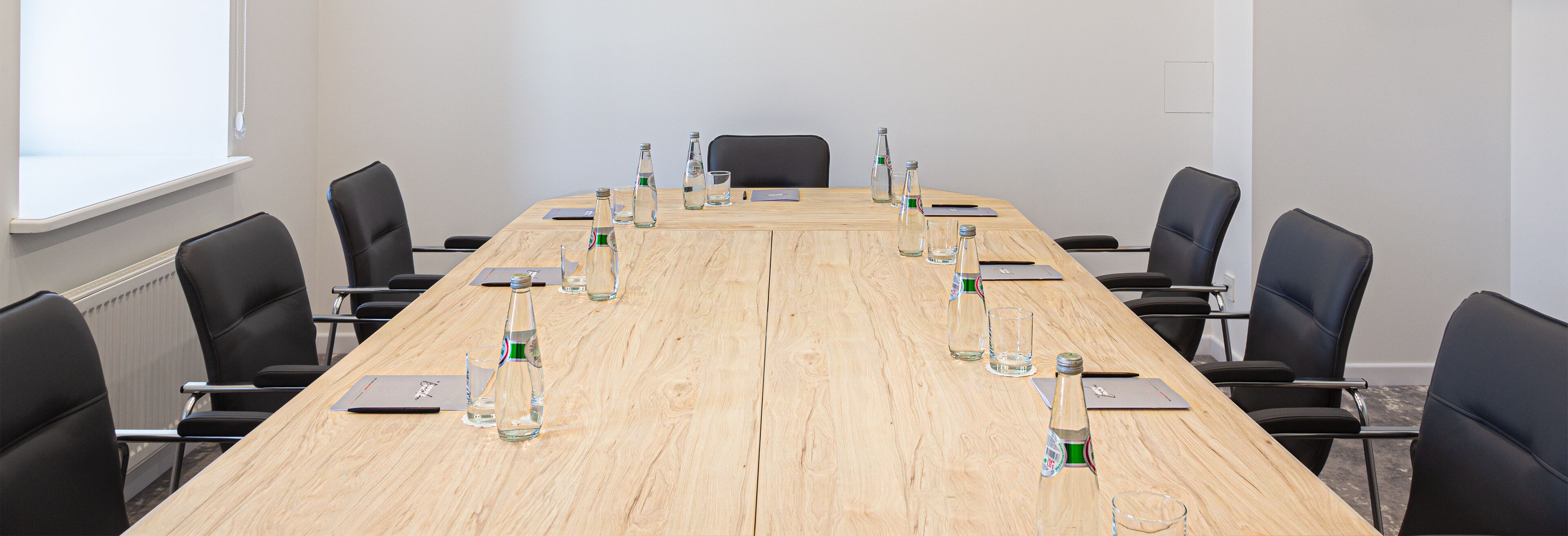 A conference room with a long wooden table, black chairs, and water bottles.