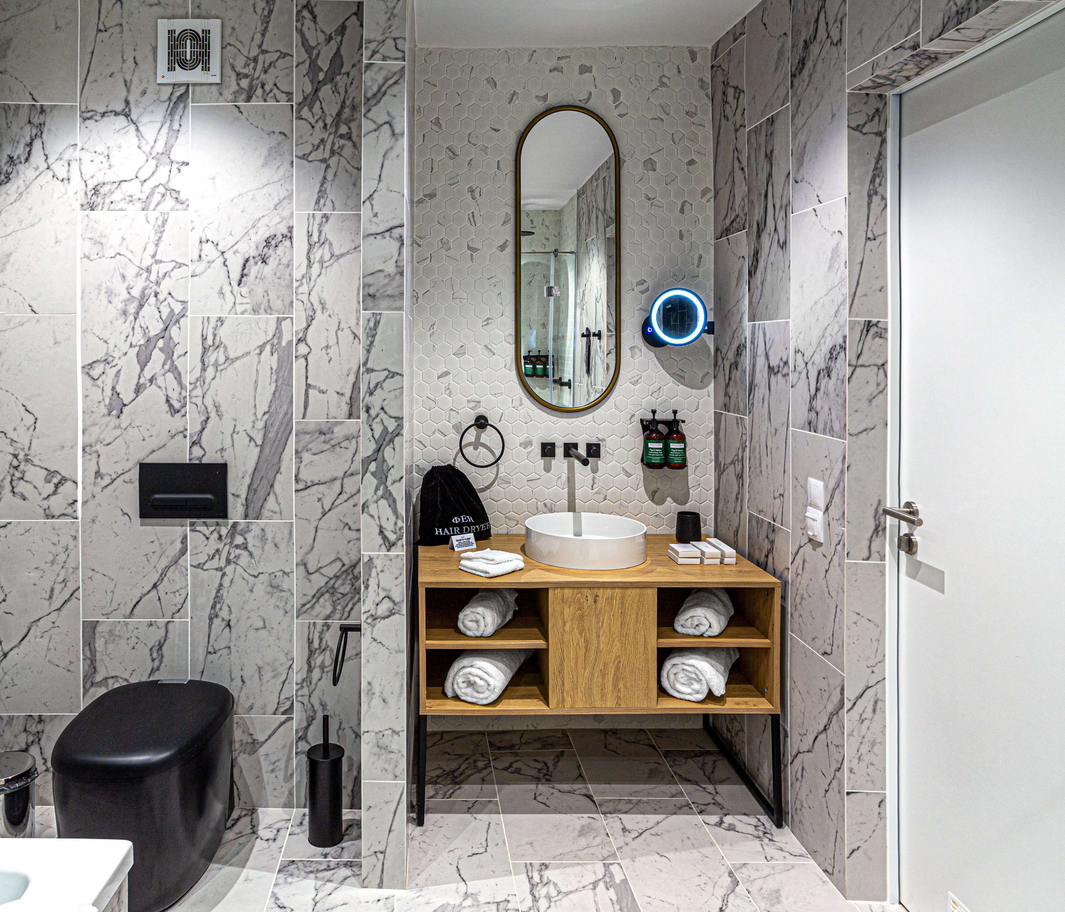 A modern bathroom with marble walls, a wooden vanity, a round mirror, and a built-in shower.
