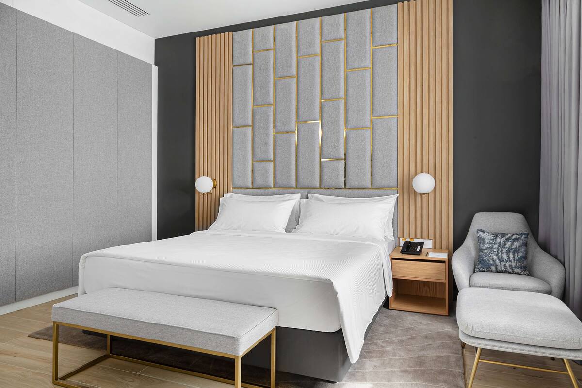A modern bedroom with a large bed, bedside tables, a bench, and a chair.