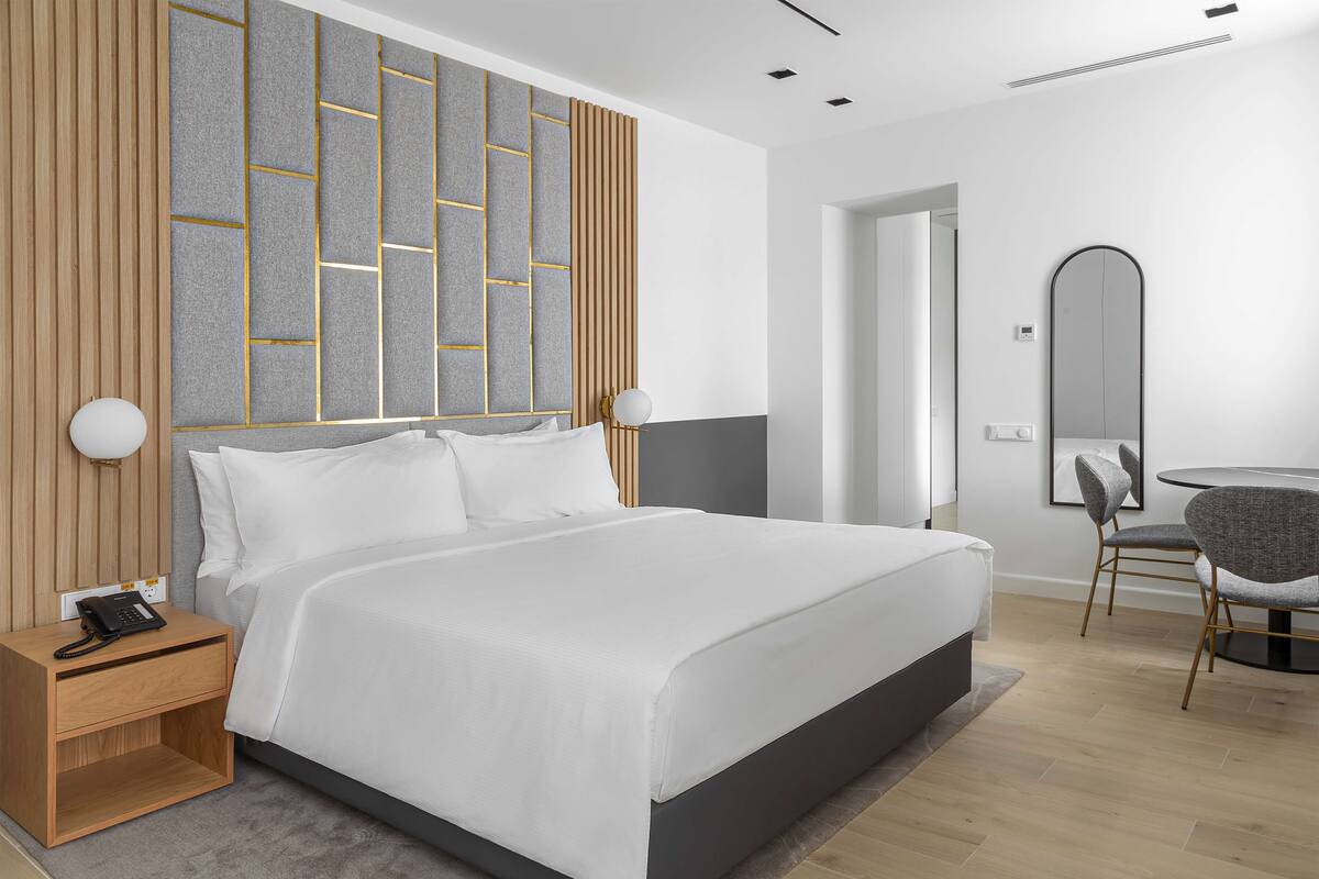 A modern hotel room with a large bed, bedside tables, a desk, and a round table with chairs.