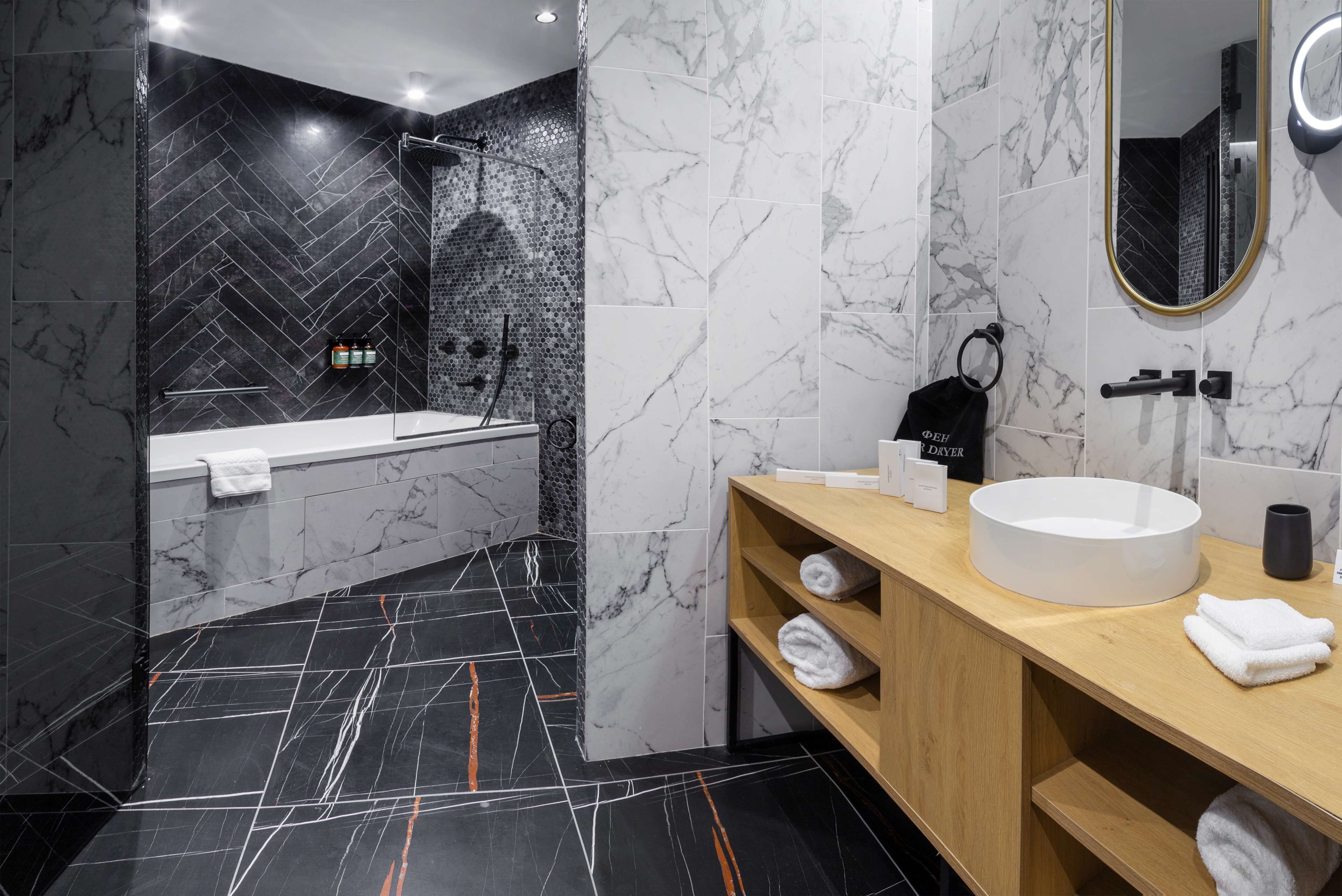 Un baño moderno con diseño de mármol blanco y negro, una bañera, un lavamanos y un espejo.