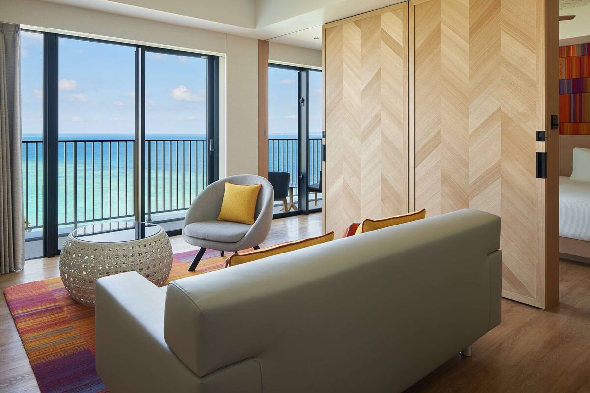 Ein modernes Hotelzimmer mit großem Balkon, einer Couch, einem Sessel und einer Holzwand.