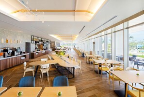 Un restaurant moderne avec un long comptoir, des tables et des chaises en bois. De grandes fenêtres se trouvent sur un des murs.