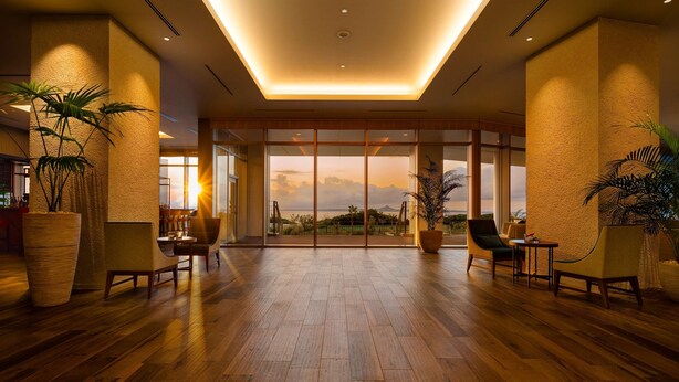 Een ruime lobby met houten vloeren, grote potplanten en uitzicht op de zonsondergang door middel van hoge glasschuurdeuren.