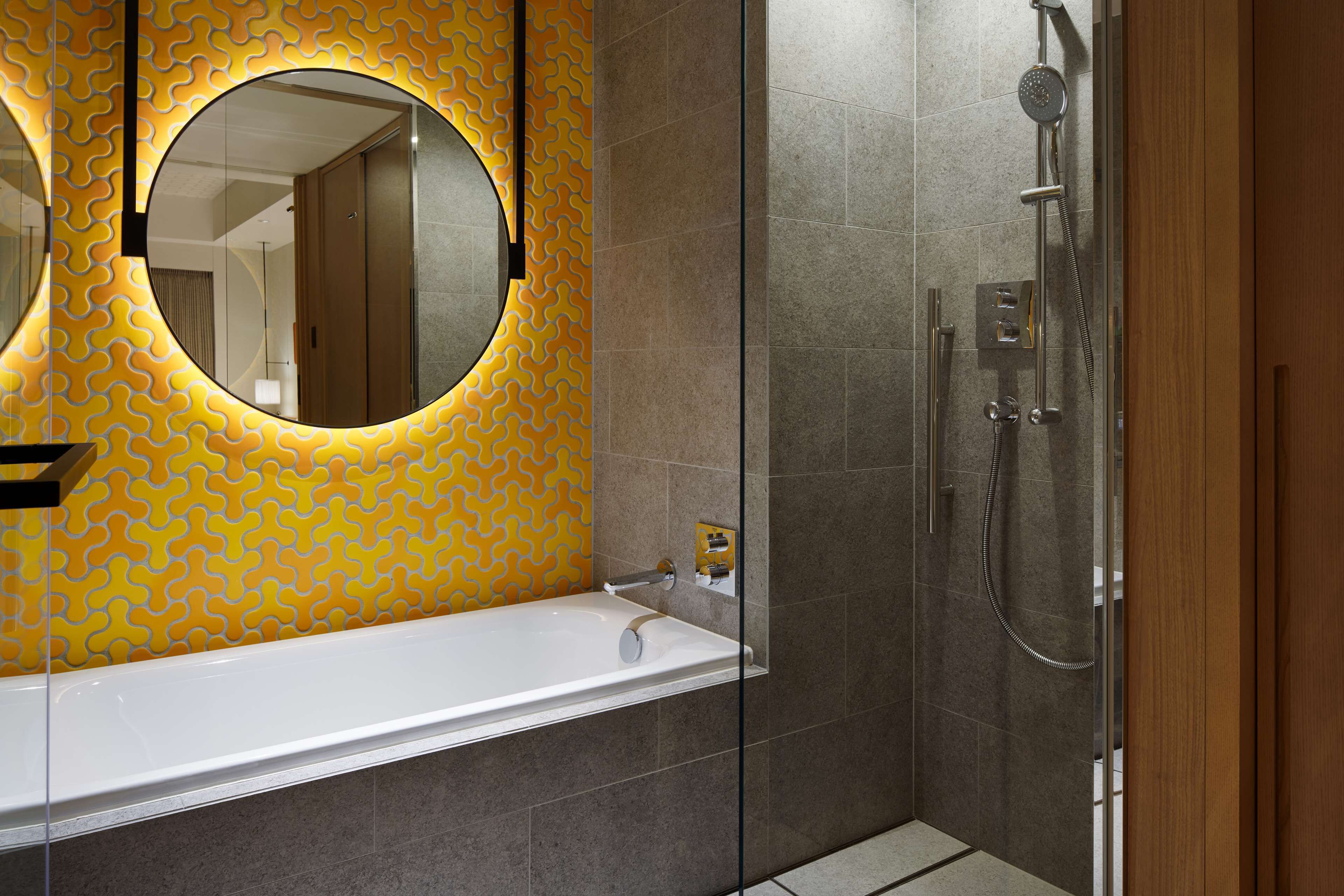 A modern bathroom with a glass-enclosed shower, a white bathtub, and a mirror with a circular frame.