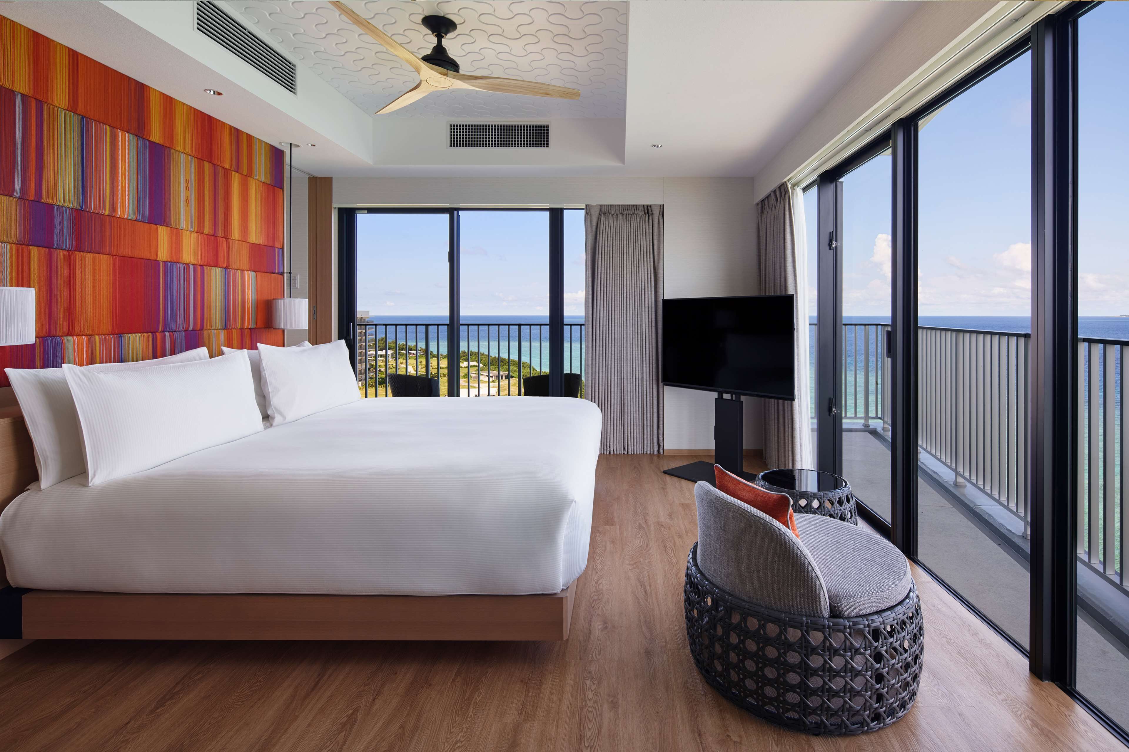 A modern hotel room with a large bed, a TV, and a view of the sea.