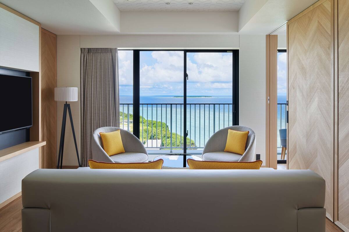 Ein modernes Hotelzimmer mit Balkon, zwei Sesseln, einem Flachbildfernseher und einem großen Fenster mit Meerblick.
