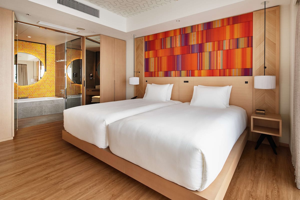 Ein modernes Hotelzimmer mit einem großen Bett, einem Badezimmer mit Spiegel und Dusche sowie einem farbenfrohen Wandbild.