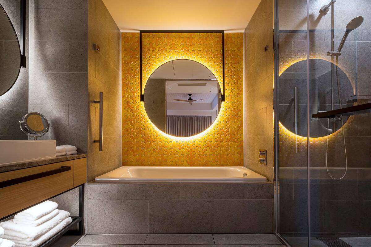 Ein modernes Badezimmer mit einer Badewanne, einem runden Spiegel und einer Dusche mit Glaswand.
