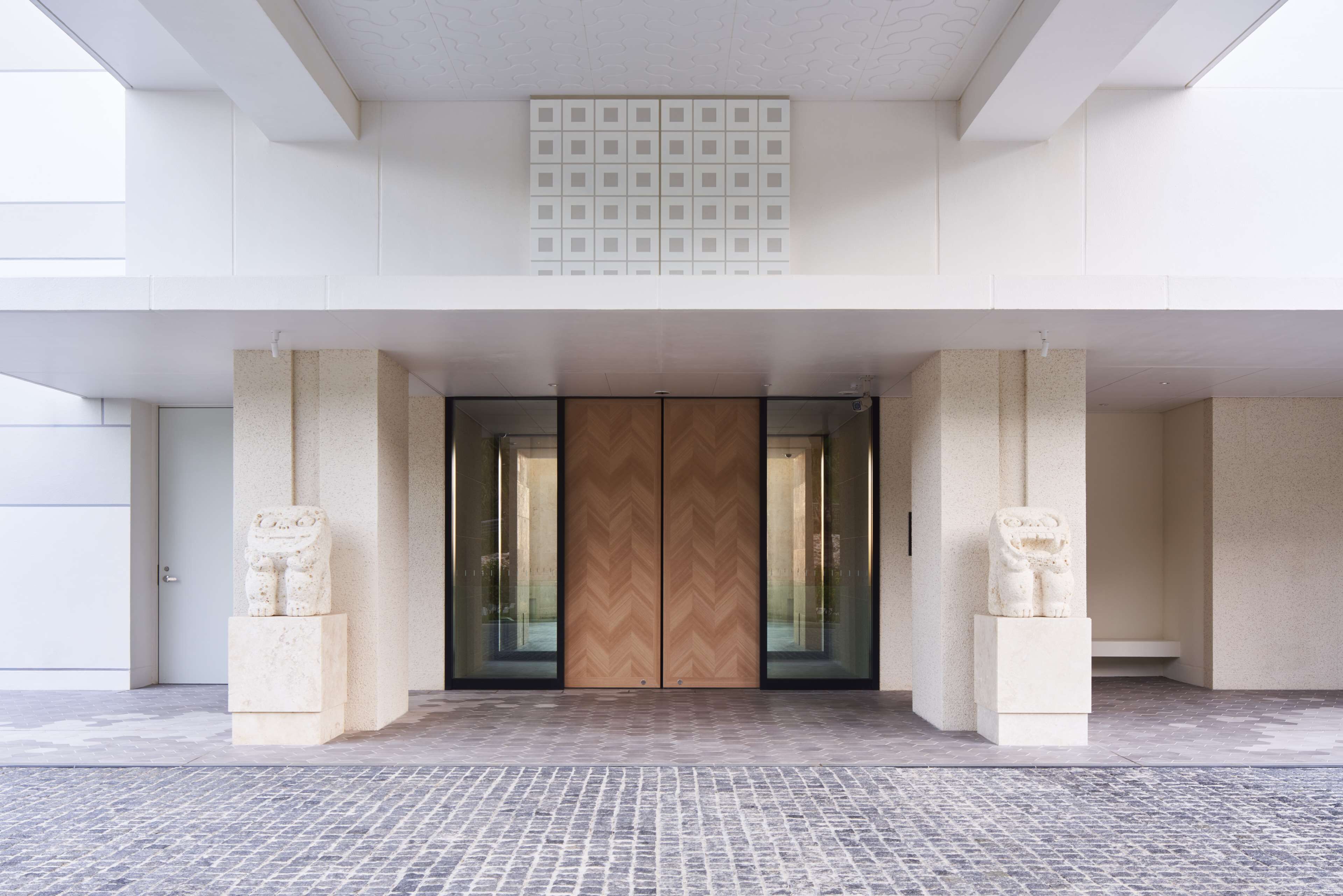 A modern building entrance with a double door, two stone statues, and a patterned floor.