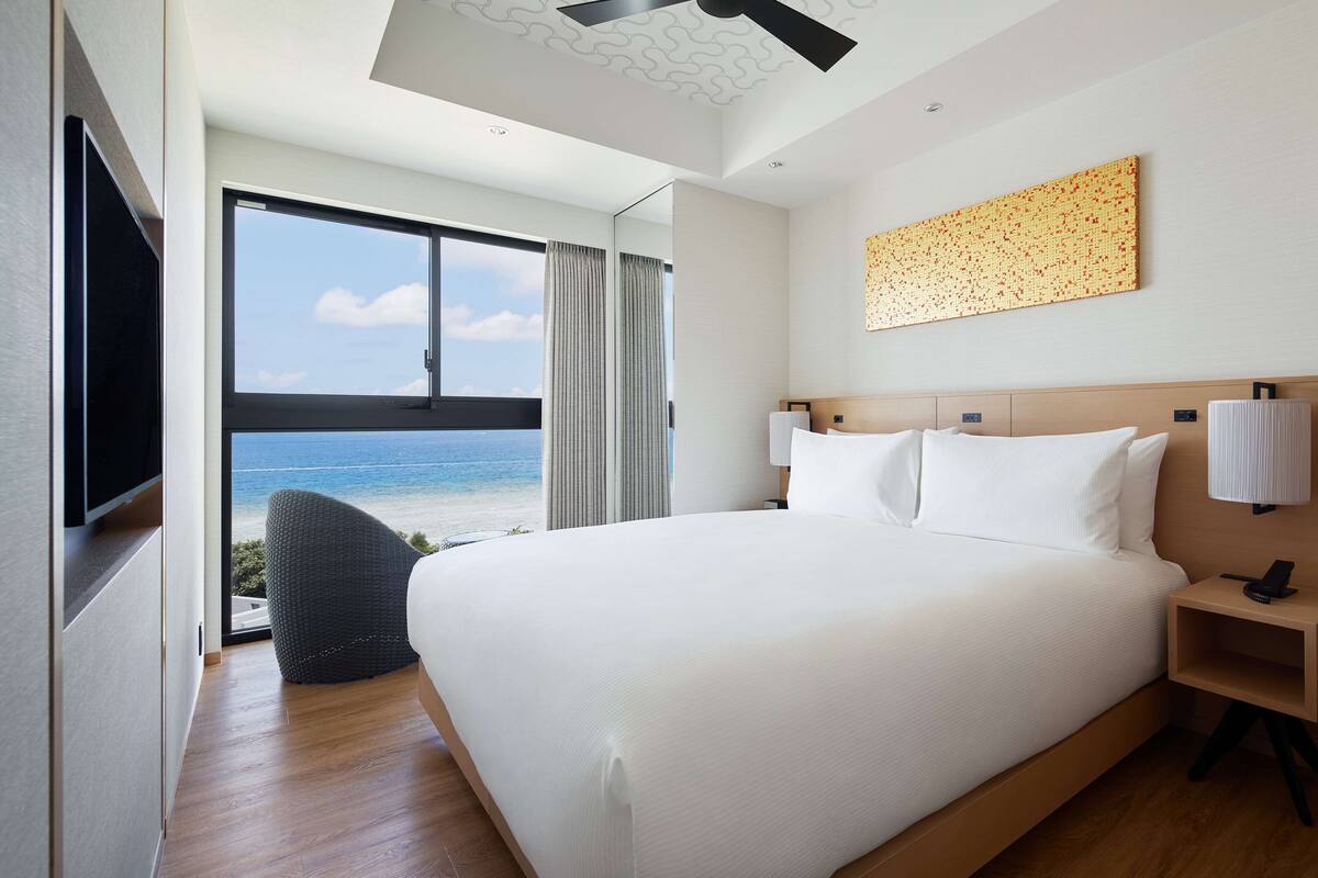 Ein modernes Hotelzimmer mit einem großen Bett, Blick auf den Strand und einem Deckenventilator.