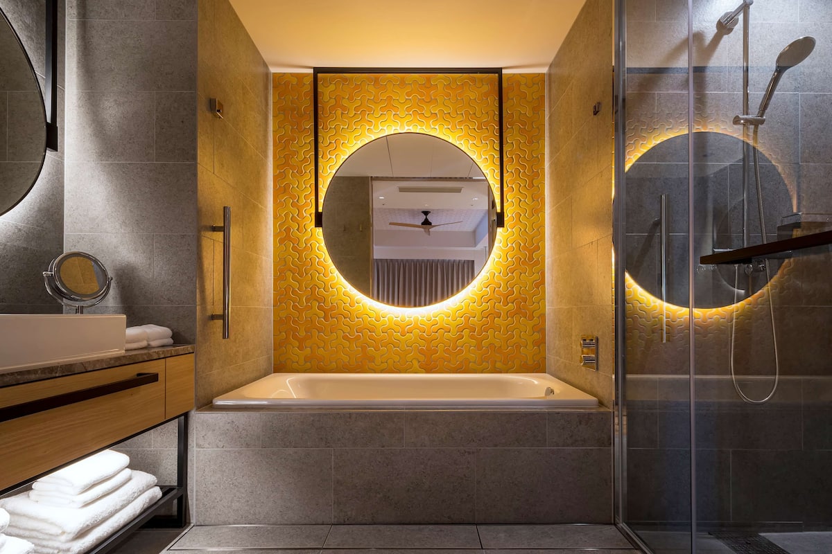Ein modernes Badezimmer mit einer Badewanne, einem runden Spiegel und einer Dusche mit Glaswand.