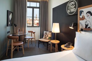 A hotel room with a bed, a round table with chairs, a lamp, a phone on a side table, and a view of the city through a window. - Se Catedral Hotel Porto, Tapestry Collection By Hilton (Porto)