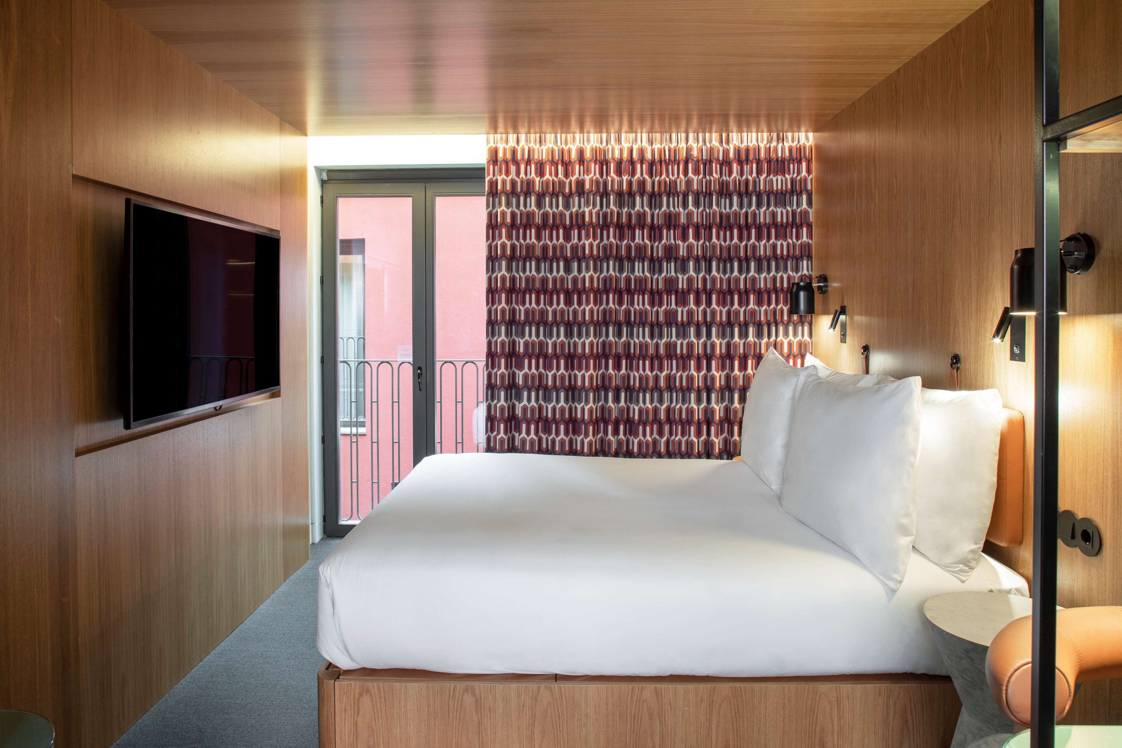 Una habitación de hotel moderna con una cama grande, un televisor de pantalla plana montado en la pared y una cortina estampada.