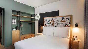Quarto de hotel com uma cama, mesa de cabeceira com luminária, guarda-roupa e placa fixada na parede.