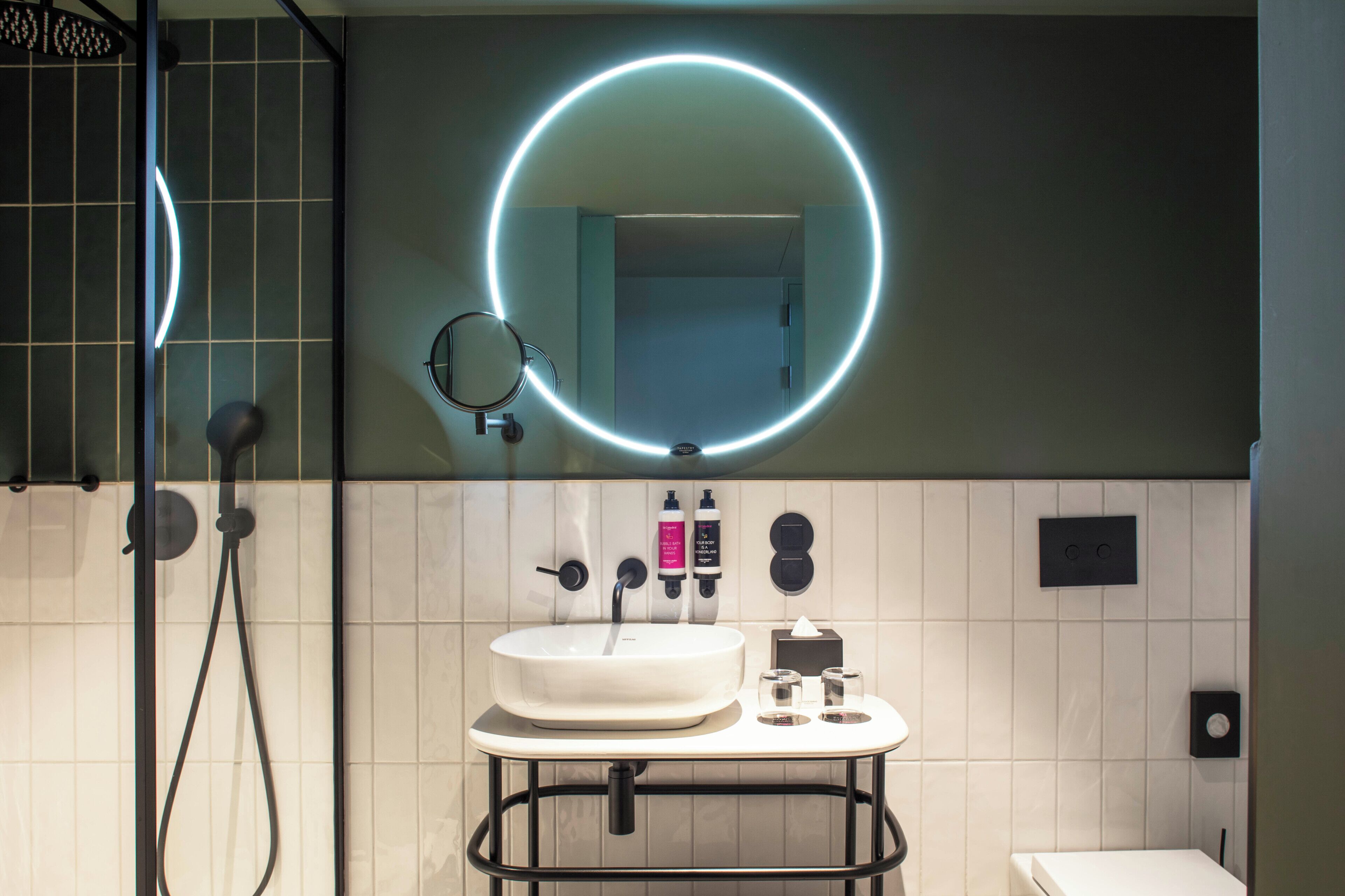 Un baño moderno con un espejo redondo, un lavamanos y una ducha.