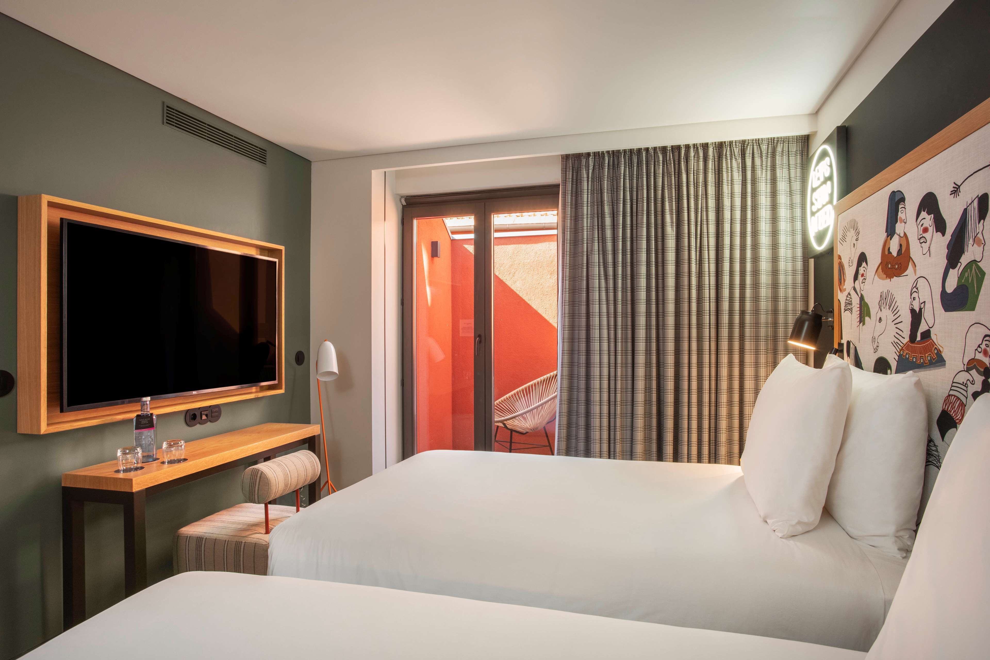 Una camera d'albergo con un letto grande, una televisione montata a parete, una scrivania con una sedia e una finestra con tende.