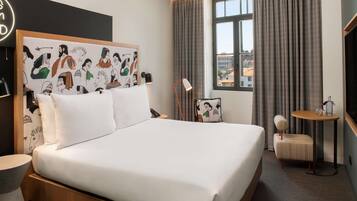 Habitación de hotel con una cama grande, una mesita de noche, una silla, una pequeña mesa, una lámpara y una ventana con cortinas.
